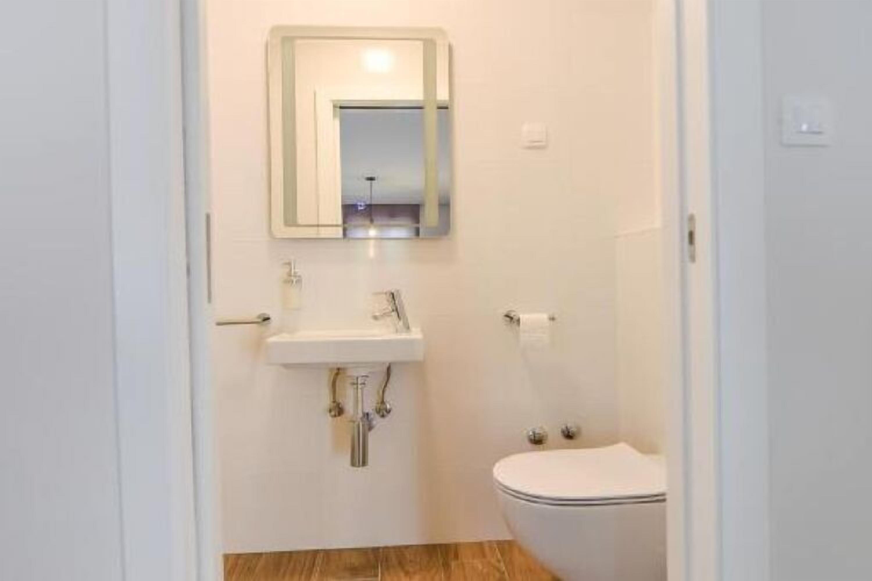 A small, clean bathroom with a white sink, mirror, and toilet.
