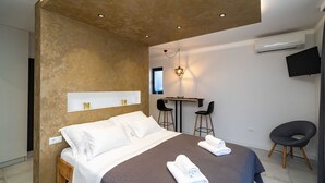 A modern hotel room with a large bed, a desk, two chairs, and a TV mounted on the wall.
