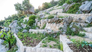 Un mur de soutènement en pierre, avec un jardin devant, une structure en bois sur une pente et des arbres en arrière-plan.
