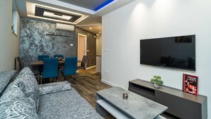 A modern living room with a sofa, a coffee table, a TV, and a dining area with chairs and a table.