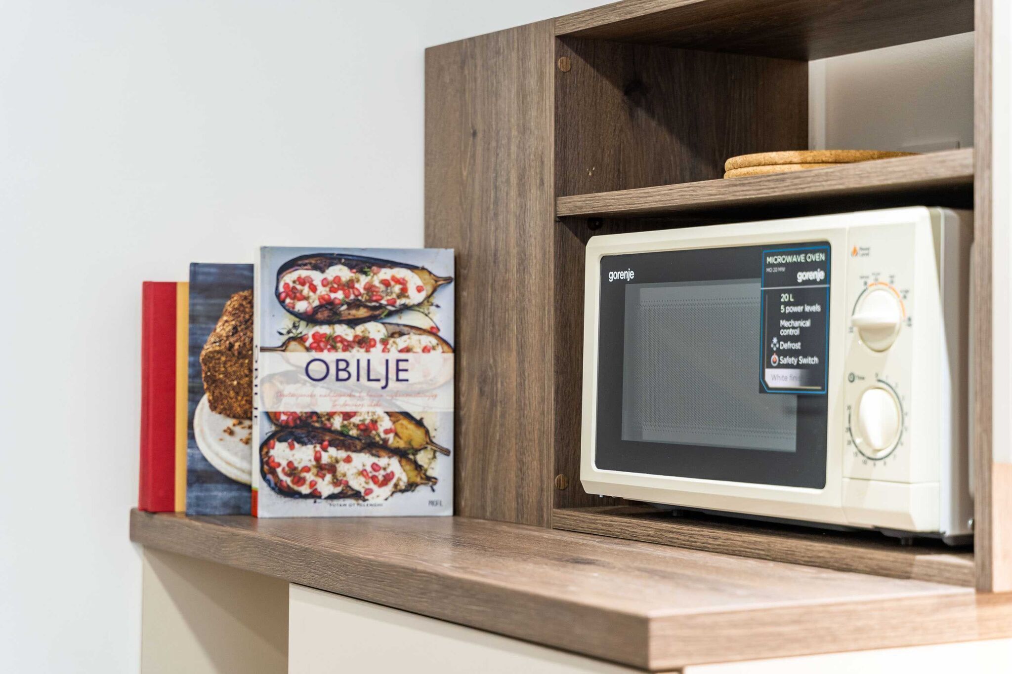 Een magnetron met digitaal display en bedieningspaneel, geplaatst op een houten plank.