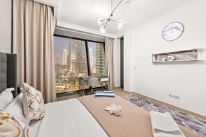 Ein Hotelzimmer mit Bett, Schreibtisch, Stuhl, Blick auf die Stadtlandschaft, einer Uhr und einem Regal mit einem Radio.