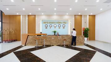 A hotel reception area with a marble floor, a reception desk, and a wall displaying clocks and a sign.