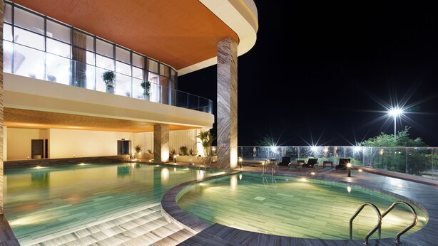 Una piscina interior moderna con diseño curvo, rodeada por una cubierta de madera y una barandilla de vidrio.