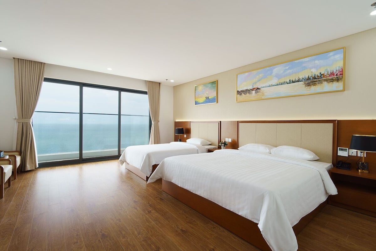 Une chambre d’hôtel avec deux lits, une grande fenêtre donnant sur la mer et un tableau accroché au mur.