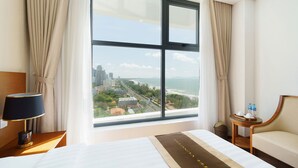 Habitación de hotel con un ventanal amplio que ofrece vistas a un paisaje urbano y la costa.