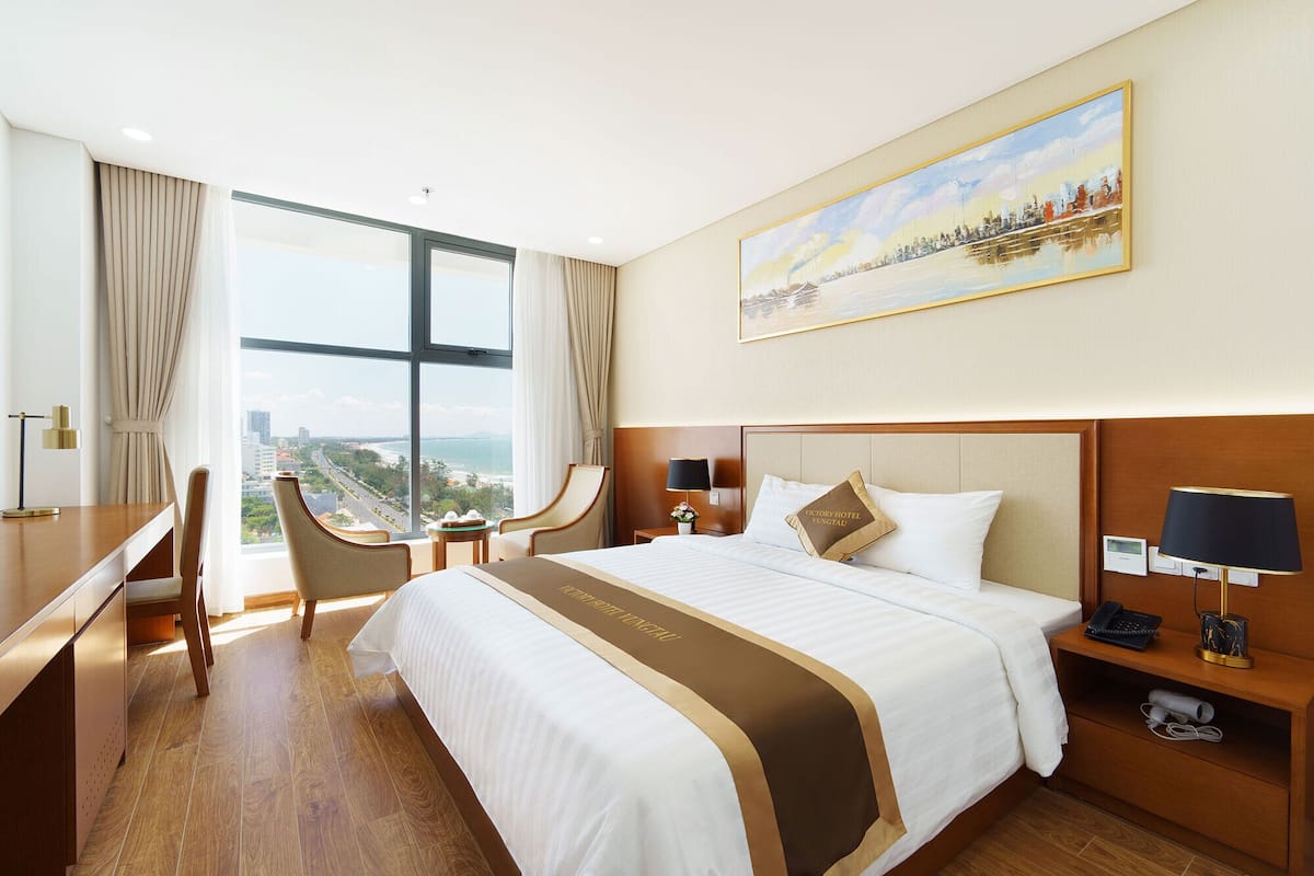 Une chambre d’hôtel avec un grand lit, un bureau, une chaise, une table de chevet et un tableau au mur.