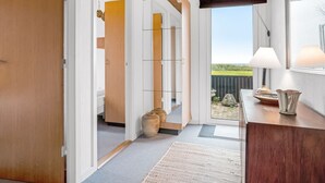 Un interior moderno con techo de madera, vista a un espacio exterior a través de un ventanal y una pequeña mesa con una lámpara.