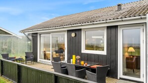 Una casa moderna con un patio amoblado, que incluye mobiliario exterior y un ventanal corredero que da a una habitación.