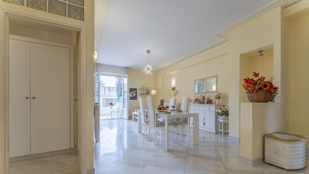 A spacious dining area with a white table and chairs, a hanging light fixture, and a basket of flowers on the wall. - Leandro's House (Montecatini Terme)