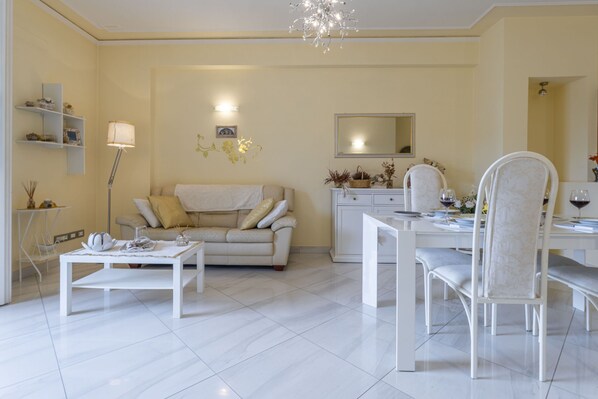 A modern living room with a sofa, coffee table, dining table, and chairs. There is a chandelier, a mirror, and shelves with decorative items. - Leandro's House (Montecatini Terme)