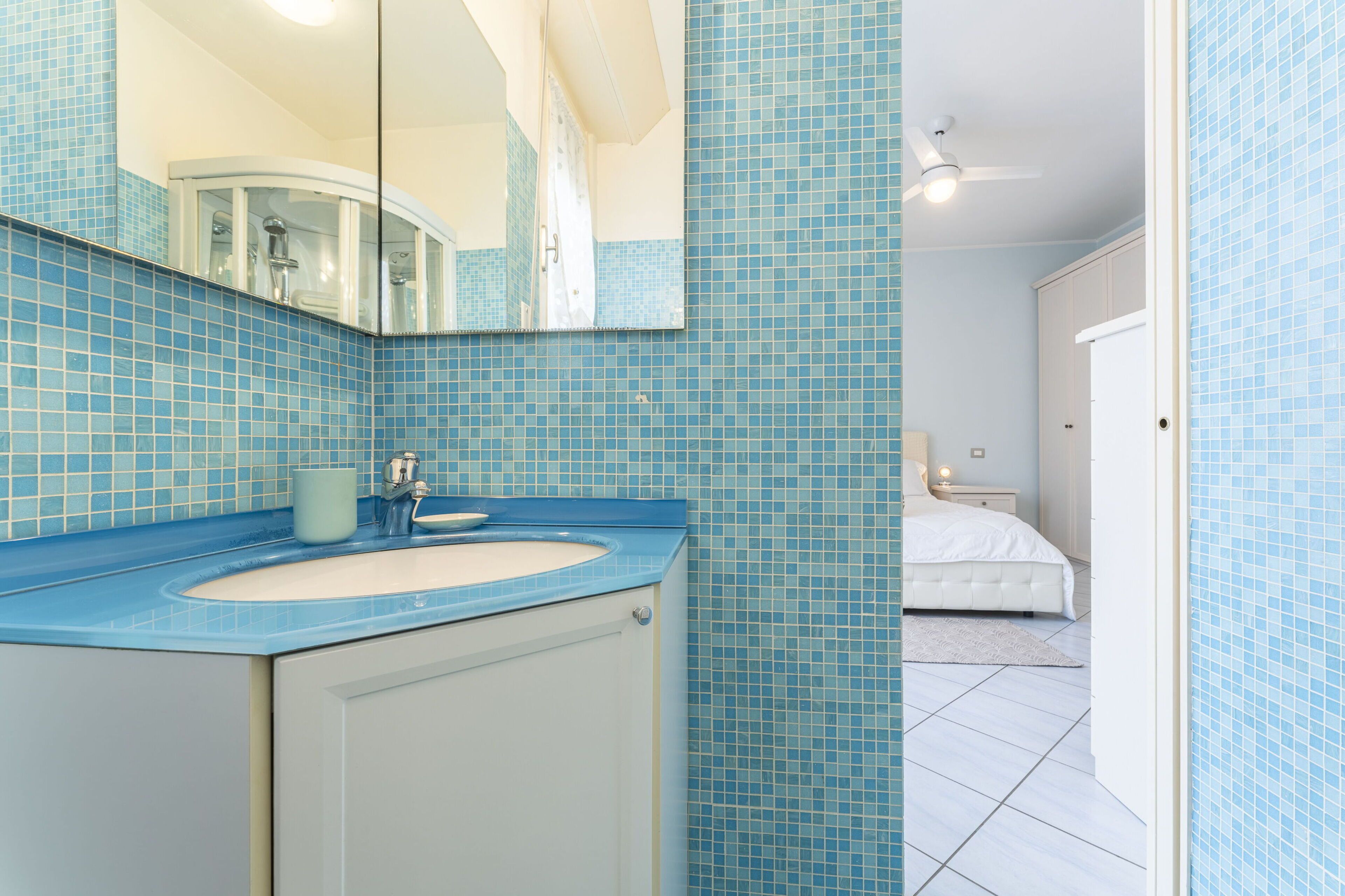 Ein Badezimmer mit blauen Fliesen, einem weißen Waschbecken und einem Spiegel.