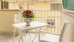 A balcony with a white table and chair, a decorative vase with flowers, and a view of the surrounding buildings. - Leandro's House (Montecatini Terme)