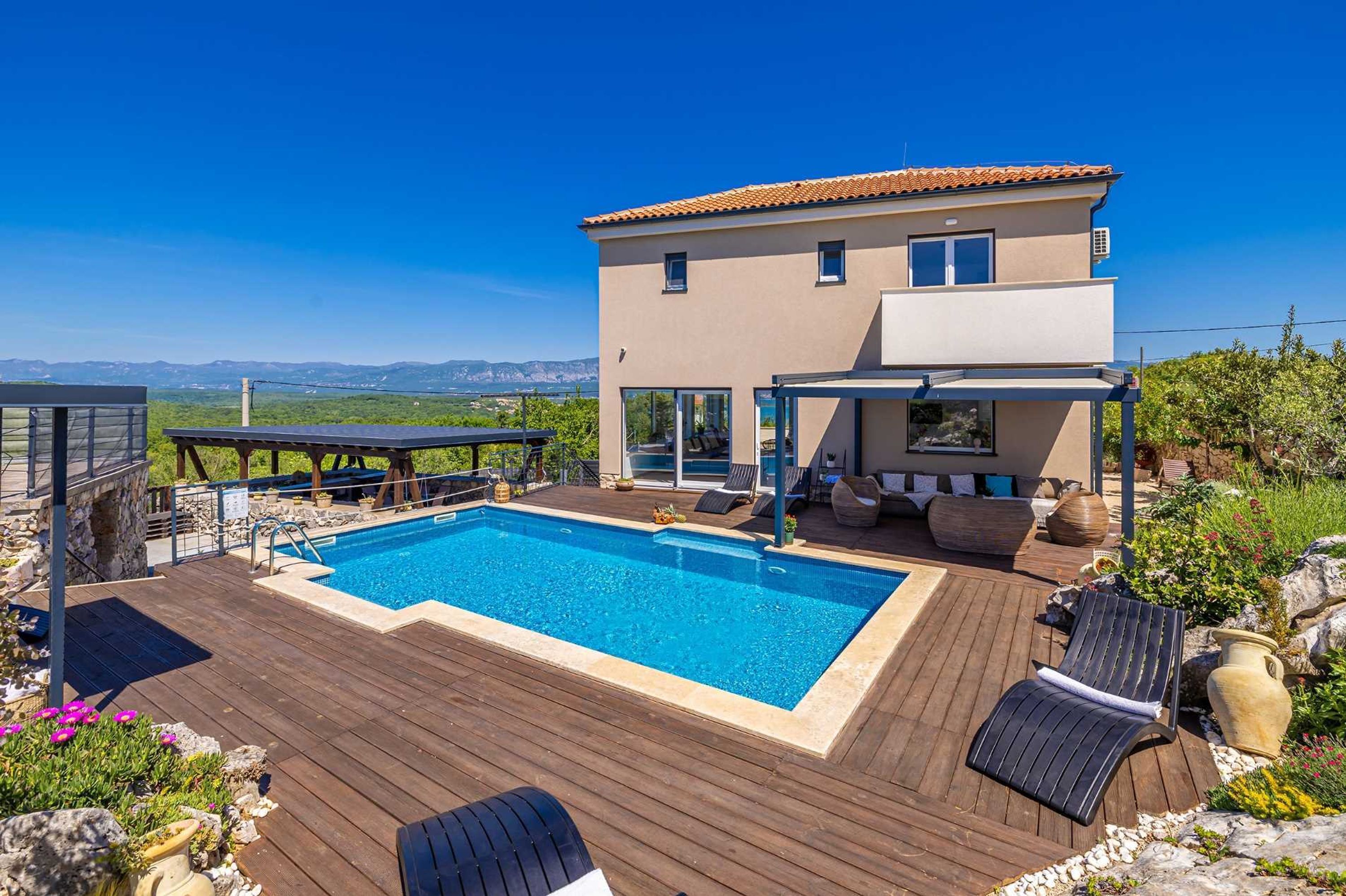 A modern villa with a swimming pool, outdoor seating, and a scenic mountain view.