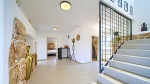 A spacious hallway with a stone wall, a staircase with a metal railing, and a bed in the background. - Villa Bella Vista in Tribulje (Dobrinj)