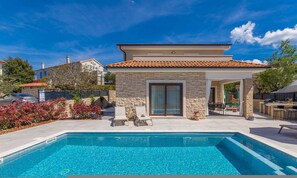 Una casa moderna con piscina, pareti in pietra e tetto in tegole.