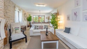 A modern living room with a stone wall, white sofas, a wooden coffee table, and a large window with natural light. - Holiday House Casa D Oro (Malinska-Dubasnica)