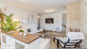 A modern living room with a white sofa, a wooden coffee table, and a TV mounted on the wall. There is a stone accent wall and a plant in the corner. - Holiday House Casa D Oro (Malinska-Dubasnica)