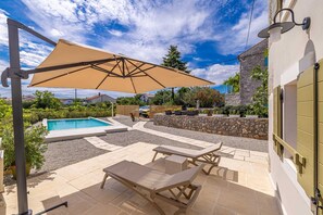 A patio with a pool, lounge chairs, and a large umbrella. - Holiday House Rural Home Frane (Krk)