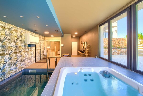 Ein modernes Badezimmer mit einer großen Badewanne, einer Duschkabine und Blick ins Freie durch große Fenster.