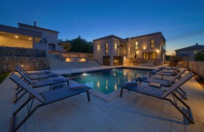 Ein moderner Poolbereich mit Liegestühlen und Schwimmbecken, umgeben von Steinmauern und zeitgenössischer Architektur.