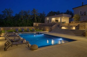 Ein moderner Poolbereich im Freien mit Liegestühlen und einer Steinmauer.
