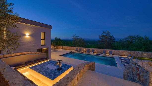 Un área de piscina moderna al aire libre con sillones de descanso y una pared de piedra.