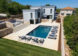 Ein modernes, zweistöckiges Haus mit Swimmingpool, Sitzgelegenheiten im Freien und einer Steinmauer.