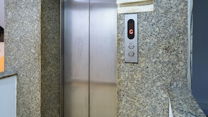 Een lift met een digitaal display en bedieningspaneel, omgeven door granieten muren en een betegelde vloer.
