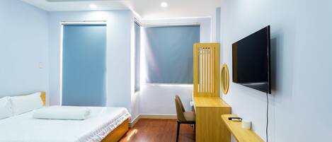 A modern hotel room with a bed, a desk, a chair, and a TV.