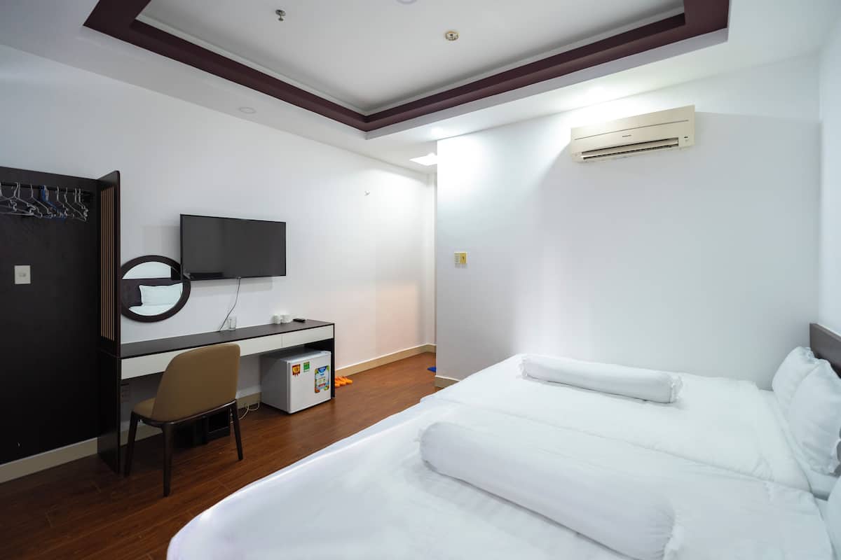 A hotel room with a bed, a desk with a chair, a television, and an air conditioning unit.