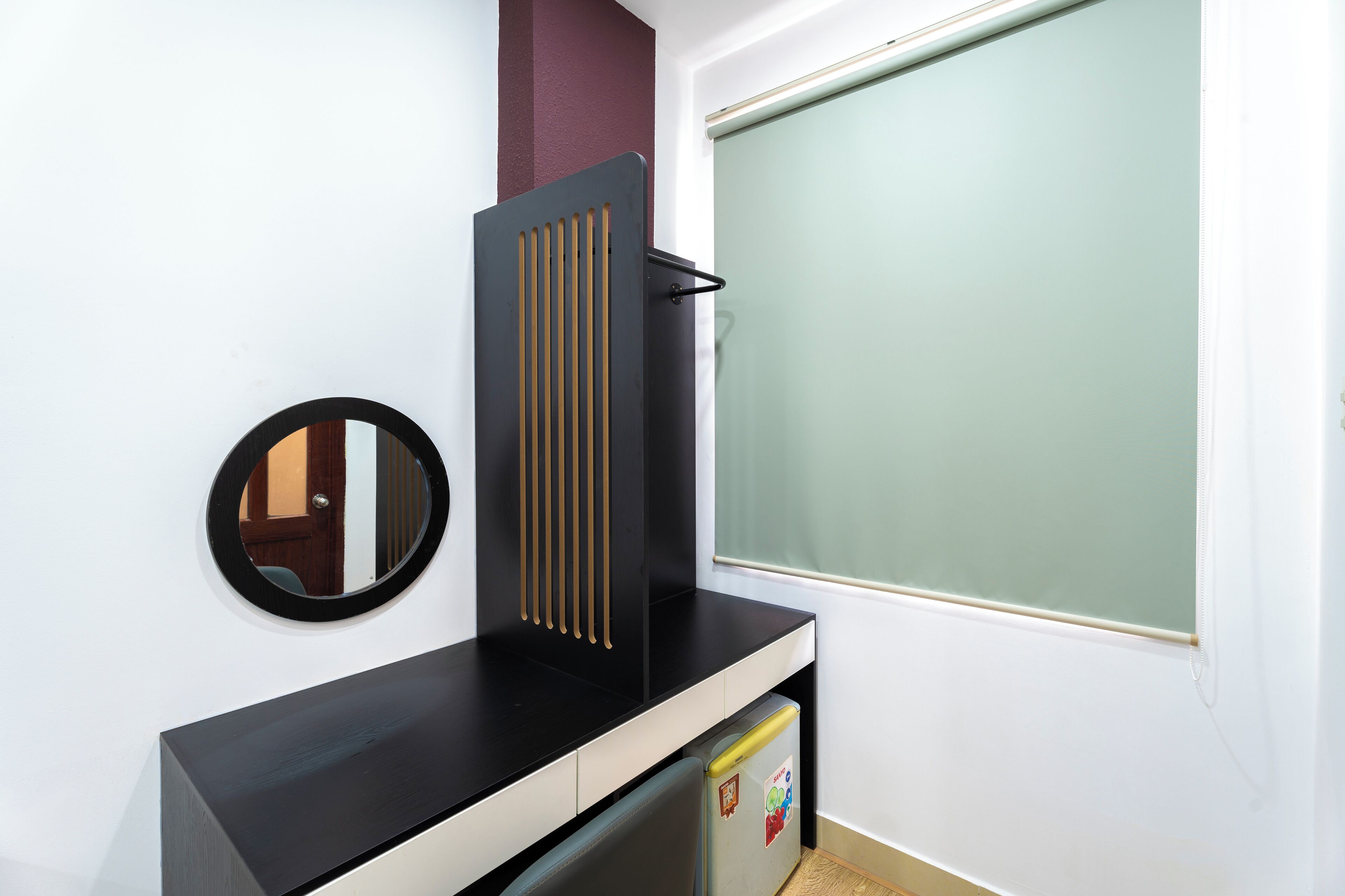Una habitación con mostrador negro, espejo, refrigerador y ventana con persiana verde.
