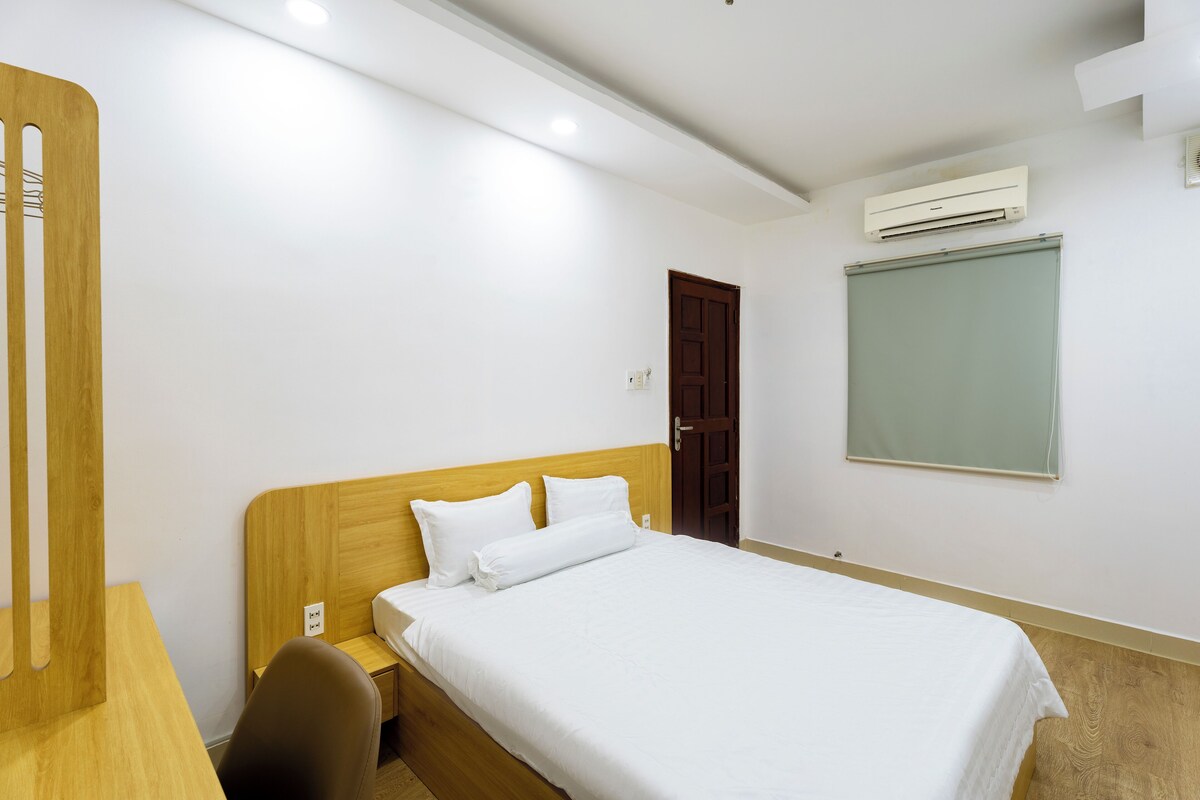 A hotel room with a wooden bed, a desk, a chair, and a window with a view.