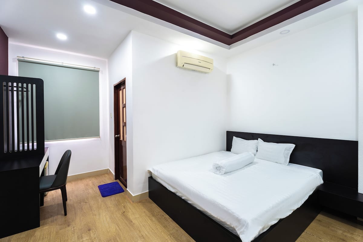 A modern bedroom with a large bed, a desk, and an air conditioning unit.