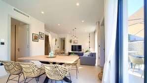 A modern living room with a wooden dining table, wicker chairs, a grey sofa, and a TV. - Villa Quarnaro With Heated Pool (Omisalj)
