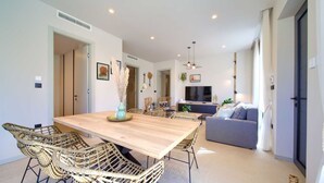 A modern living room with a wooden dining table, wicker chairs, a grey sofa, and a TV. - Villa Quarnaro With Heated Pool (Omisalj)