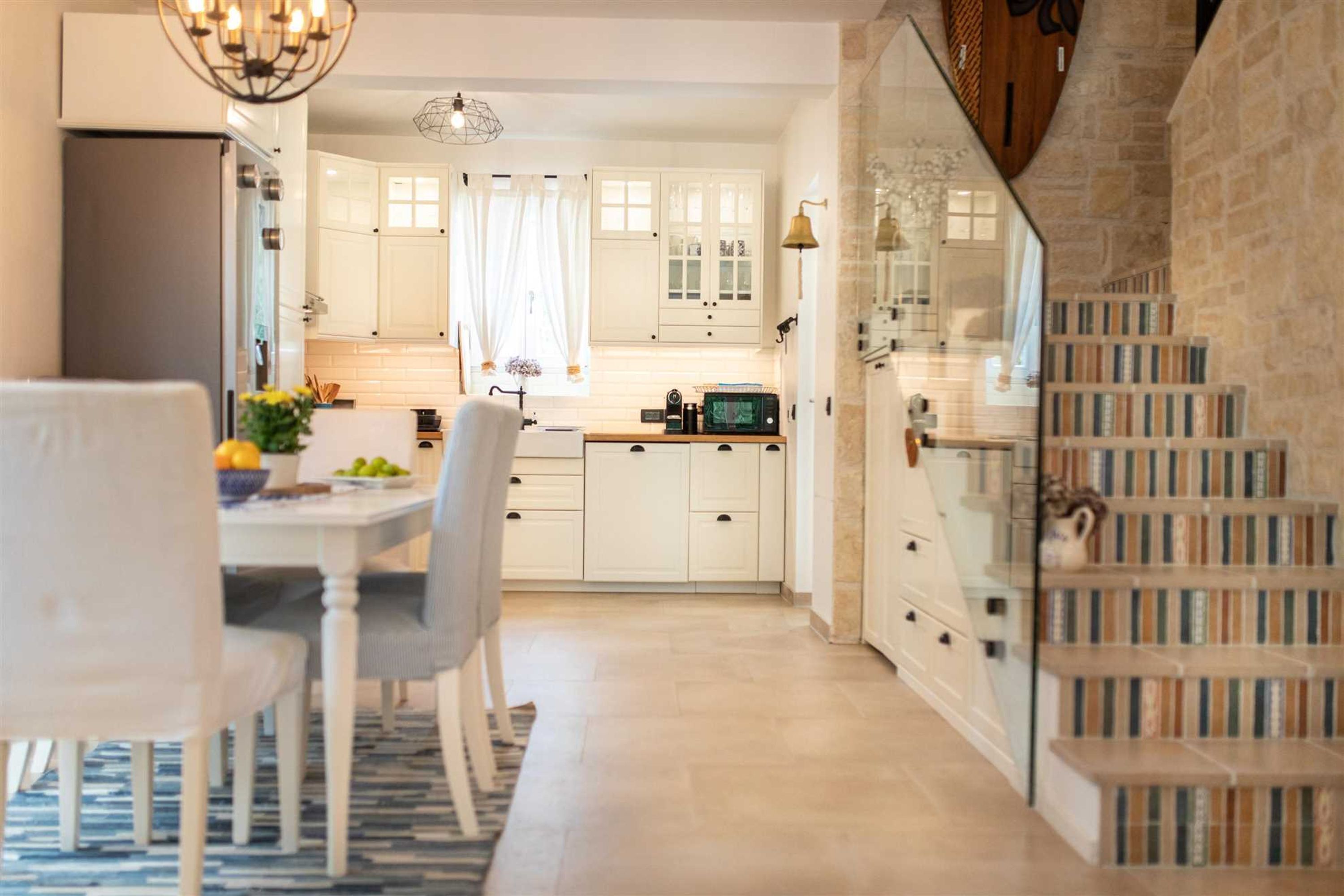 A modern kitchen with white cabinets, a dining table with chairs, and a staircase with bookshelves.