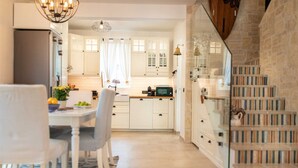 A modern kitchen with white cabinets, a dining table with chairs, and a staircase with bookshelves. - Villa Gita in Malinska (Malinska-Dubasnica)