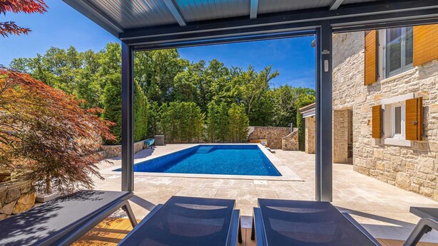 A modern outdoor pool area with lounge chairs, a stone building, and a view of trees. - Villa Gita in Malinska (Malinska-Dubasnica)
