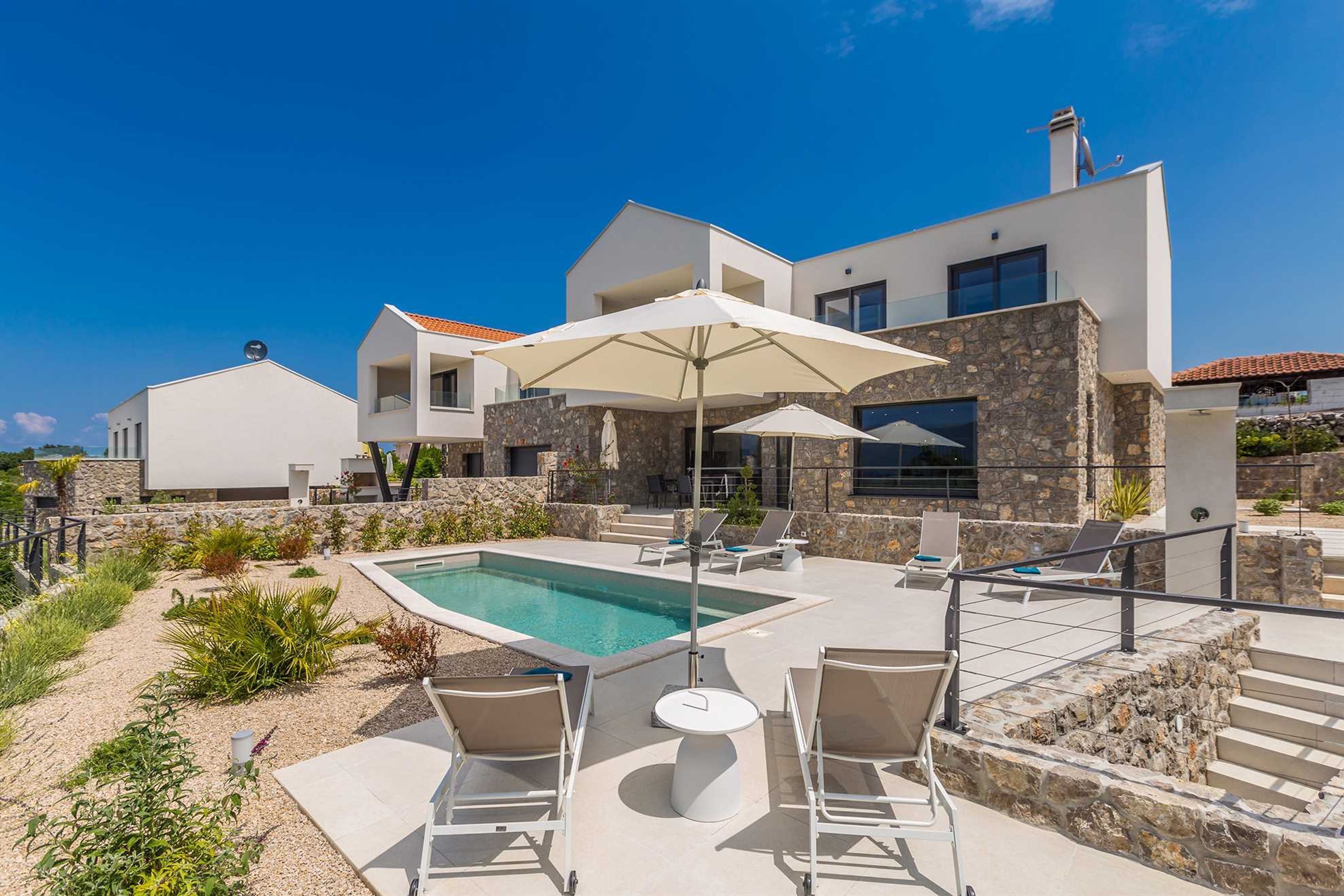 A modern house with a swimming pool, outdoor seating, and a stone facade.