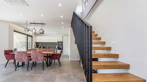 A modern kitchen with dark cabinets, a dining area with a wooden table and chairs, and a staircase with wooden steps and a black railing. - Villa Verena With Heated Pool (Krk)