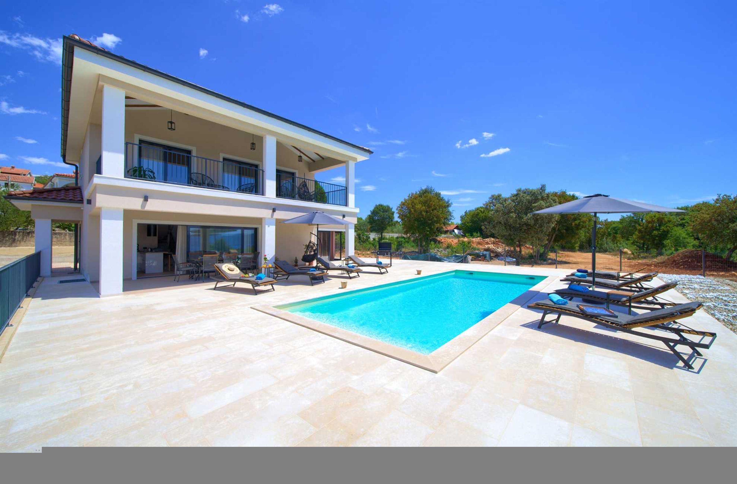 Une maison moderne à deux étages, dotée d’une piscine, de chaises longues et d’un patio couvert.