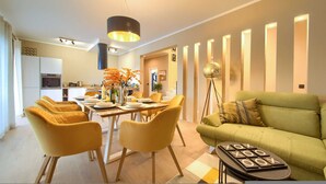 A modern living room with a green sofa and yellow chairs, a dining area with a table set for four, and a kitchen in the background. - Villa Magnifica in Pinezici (Krk)