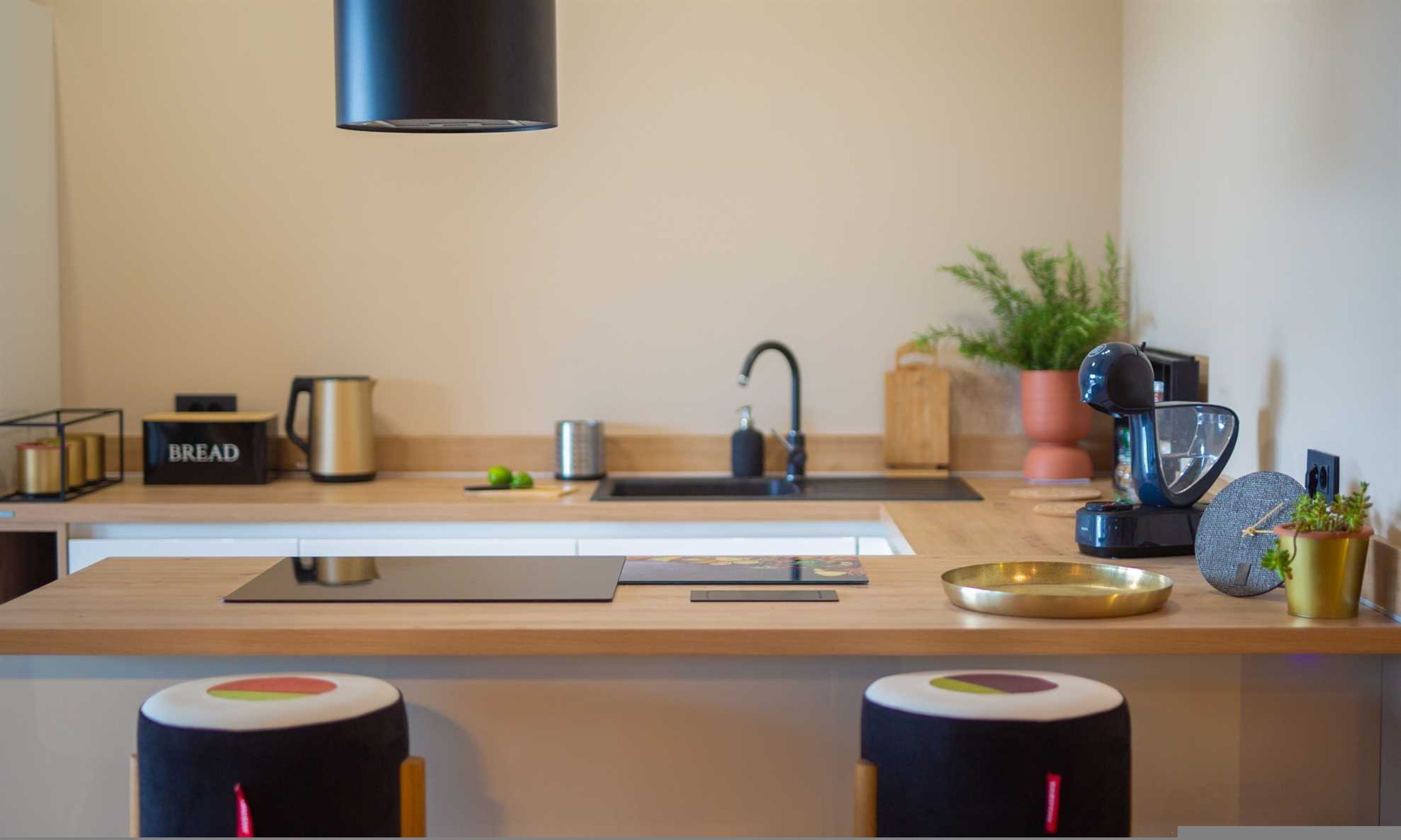A modern kitchen with a wooden countertop, a stainless steel kettle, a bread box, a coffee maker, and a potted plant.