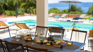A dining table set with food and drinks, overlooking a pool and lounge chairs. - Villa Magnifica in Pinezici (Krk)