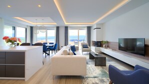 A modern living room with a sofa, chairs, a TV, and a kitchen area with a dining table. - Villa Majestic With Sauna and Beautiful Views (Vrbnik)