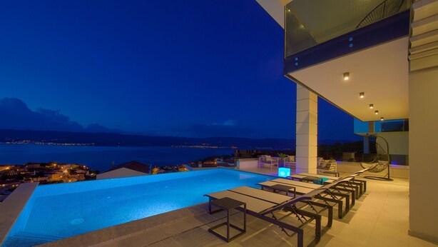 A modern infinity pool with a view of the sea and mountains at dusk. - Villa Majestic With Sauna and Beautiful Views (Vrbnik)