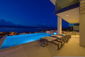 A modern infinity pool with a view of the sea and mountains at dusk. - Villa Majestic With Sauna and Beautiful Views (Vrbnik)