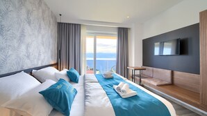 A modern hotel room with a large bed, a TV mounted on the wall, and a balcony with a view of the sea. - Villa Majestic With Sauna and Beautiful Views (Vrbnik)