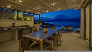 A modern outdoor dining area with a view of the sea at dusk. - Villa Majestic With Sauna and Beautiful Views (Vrbnik)